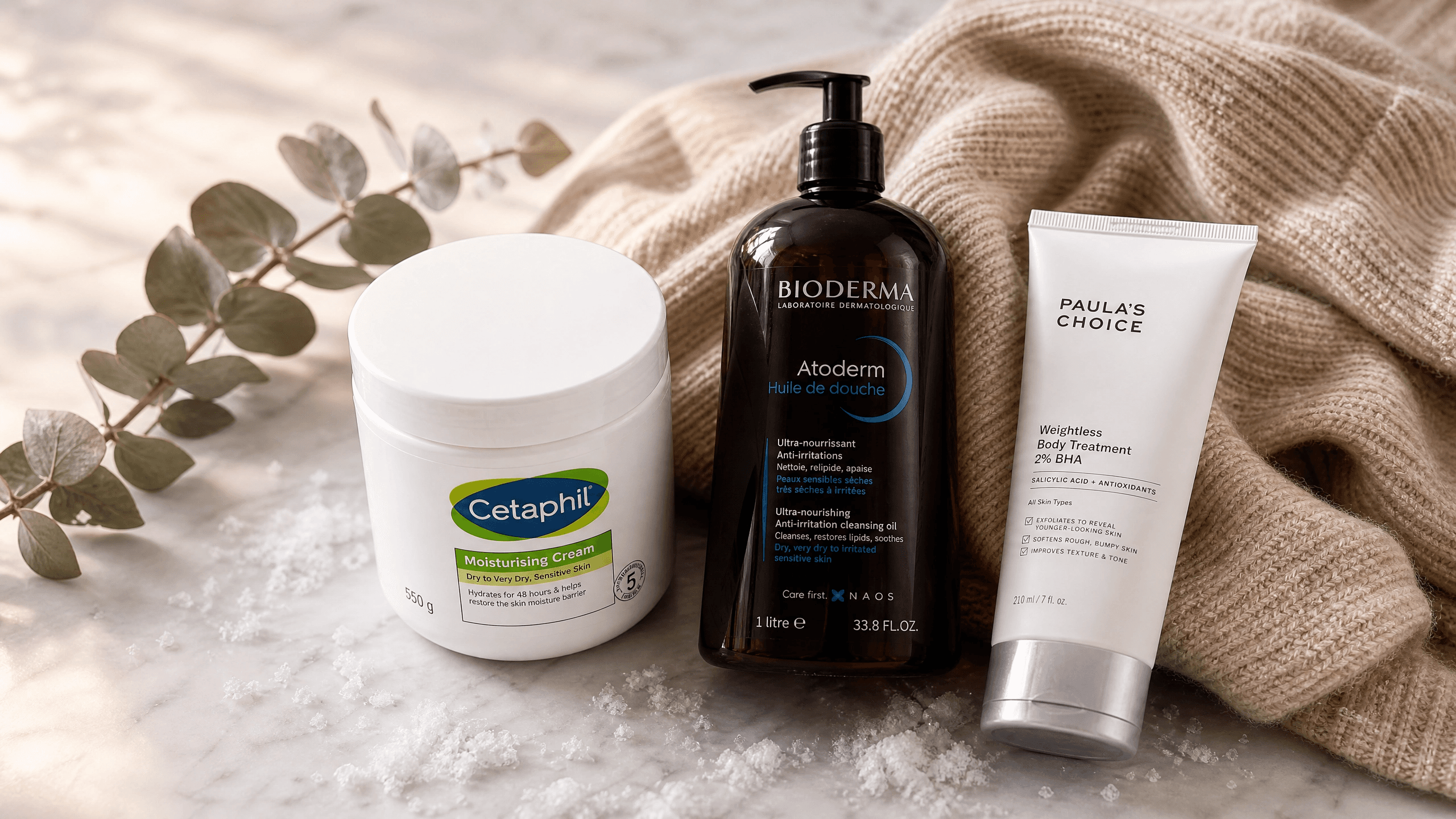 A luxurious editorial flat lay of rich body creams, oils, and exfoliants on a marble surface with soft winter lighting