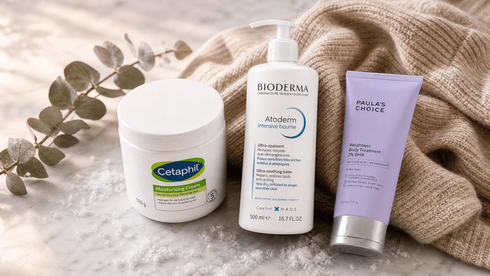 A luxurious editorial flat lay of rich body creams, oils, and exfoliants on a marble surface with soft winter lighting